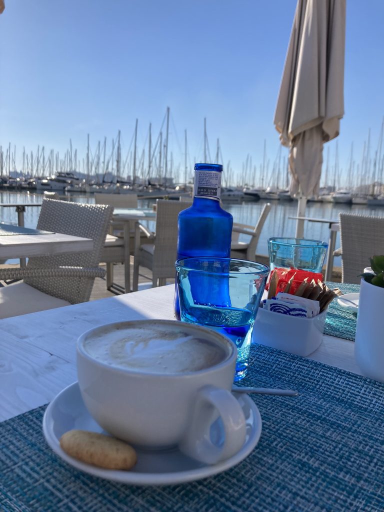 Kaffeetasse und blaue Wasserflasche auf einem Tisch im Hafencafé, Palma